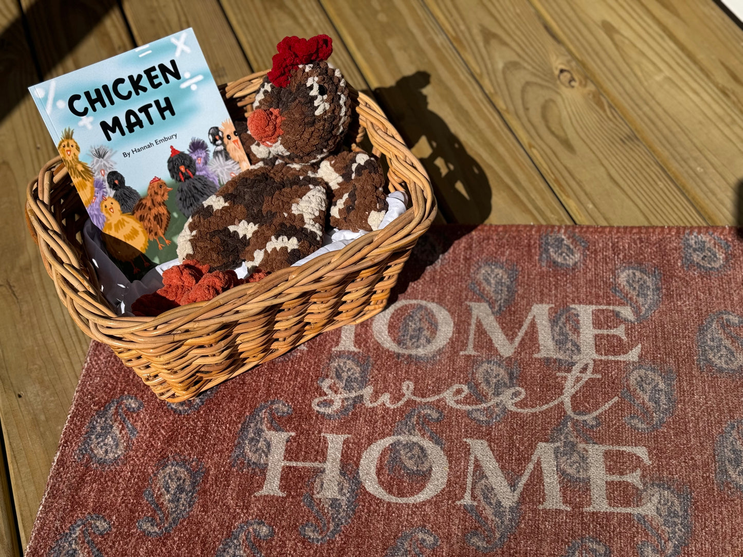 Basket with toys and a book titled 'Chicken Math' on a doormat with 'Home Sweet Home' text.