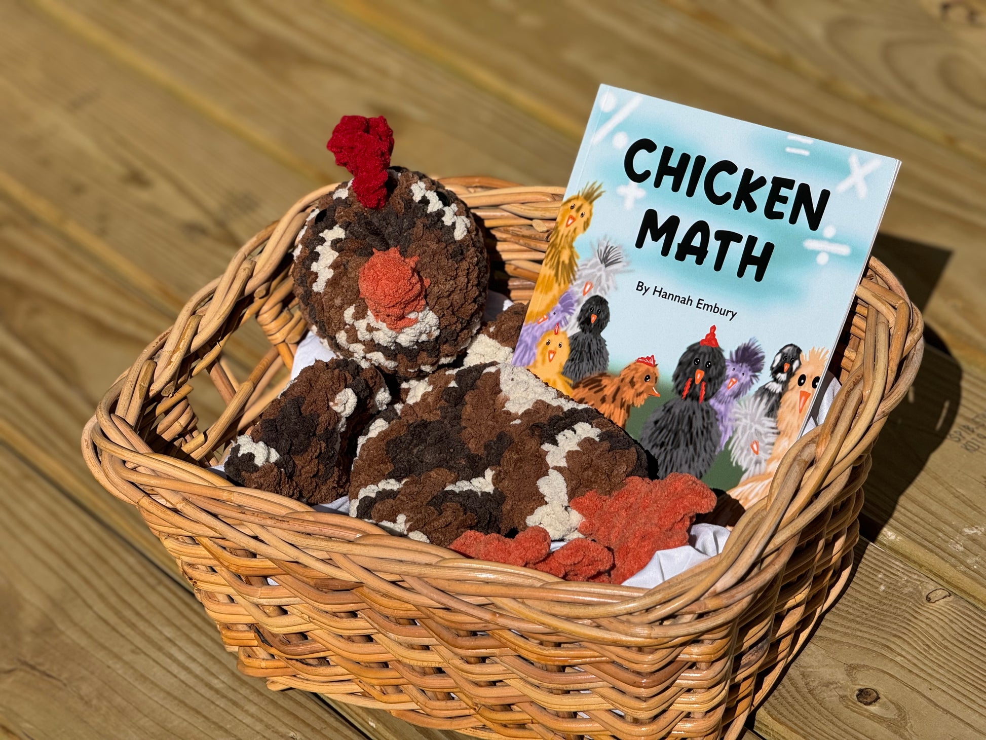 Wicker basket with a plush chicken toy and a book titled 'Chicken Math' on a wooden surface.