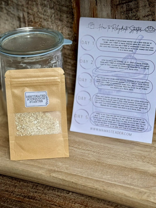 Glass jar with a brown paper bag containing dehydrated sourdough starter, next to a printed sheet on a wooden surface.