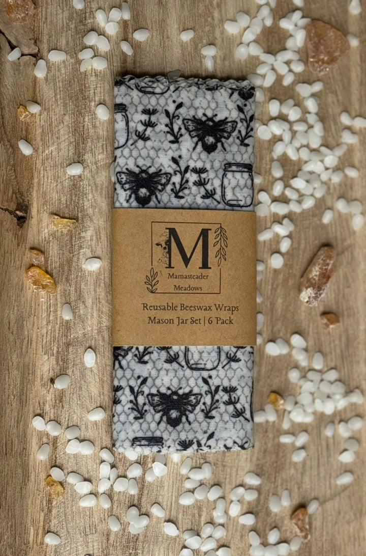 Reusable beeswax wraps with a brand label on a wooden surface with beeswax pellets
